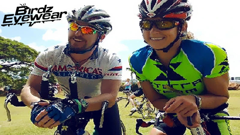 Two cyclists in colorful gear smile while leaning on their bikes. They wear helmets and sunglasses. Two cyclists in colorful gear smile while leaning on their bikes. They wear helmets and sunglasses.