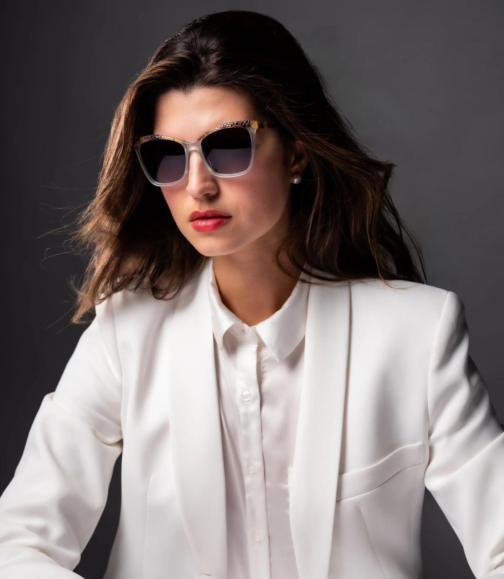 A woman in a white suit poses confidently against a dark background, wearing Di Valdi DV0158 Sunglasses from Di Valdi that feature cat eye frames and UV protection. A woman in a white suit poses confidently against a dark background, wearing Di Valdi DV0158 Sunglasses from Di Valdi that feature cat eye frames and UV protection.