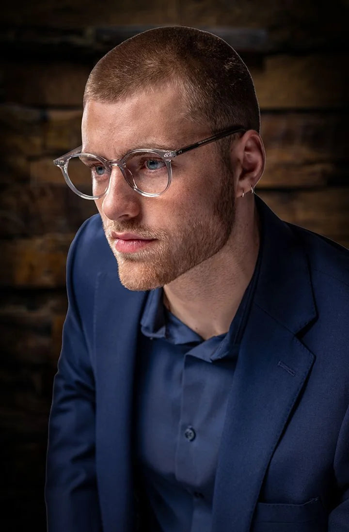 Man with short hair, glasses, and an earring, wearing a navy suit and shirt, looks thoughtfully to the side in Di Valdi DVO8187 Eyeglasses | Size 47—prescription-ready style from Di Valdi. Man with short hair, glasses, and an earring, wearing a navy suit and shirt, looks thoughtfully to the side in Di Valdi DVO8187 Eyeglasses | Size 47—prescription-ready style from Di Valdi.