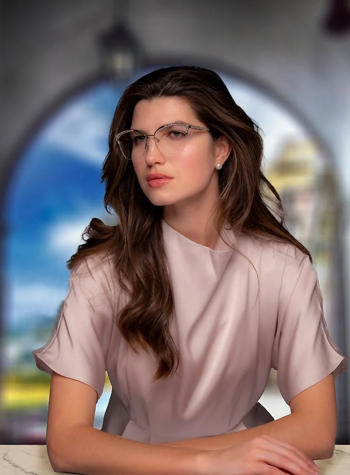 A woman with long brown hair and glasses sits at a table in a pale pink blouse, wearing stylish Di Valdi DVO8190 Eyeglasses (Size 54) by Di Valdi, with a blurred background. A woman with long brown hair and glasses sits at a table in a pale pink blouse, wearing stylish Di Valdi DVO8190 Eyeglasses (Size 54) by Di Valdi, with a blurred background.