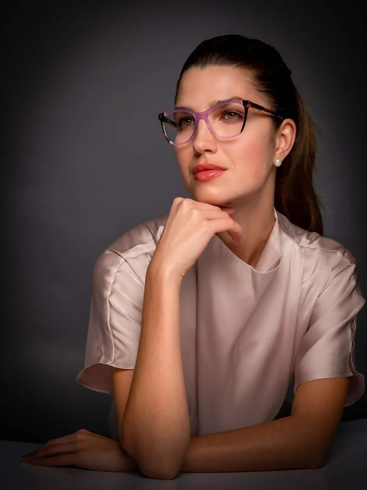 A woman wearing Di Valdi DVO8195 Eyeglasses with square rims and acetate temples poses thoughtfully, resting her chin on her hand against a dark background. A woman wearing Di Valdi DVO8195 Eyeglasses with square rims and acetate temples poses thoughtfully, resting her chin on her hand against a dark background.
