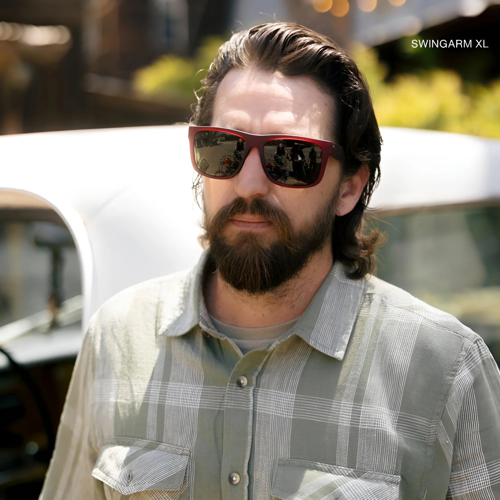 Confidently standing in front of a car, a bearded man rocks a plaid shirt and Electric's stylish Jason Momoa Swingarm M Sunglasses | Size 57, offering excellent UV protection. Confidently standing in front of a car, a bearded man rocks a plaid shirt and Electric's stylish Jason Momoa Swingarm M Sunglasses | Size 57, offering excellent UV protection.