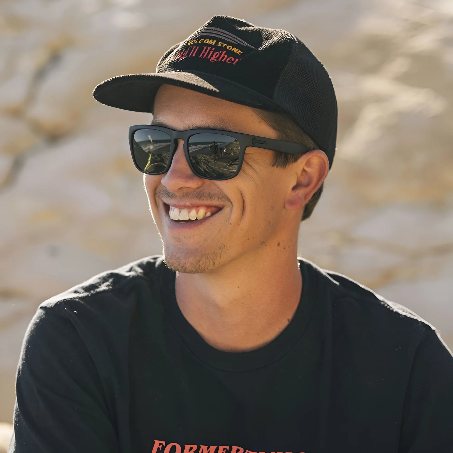 A smiling man wears Electric Knoxville XL Sunglasses | Size 61 by Electric and a black cap while sitting outdoors in bright sunlight, enjoying superior sun protection and a lightweight fit. A smiling man wears Electric Knoxville XL Sunglasses | Size 61 by Electric and a black cap while sitting outdoors in bright sunlight, enjoying superior sun protection and a lightweight fit.