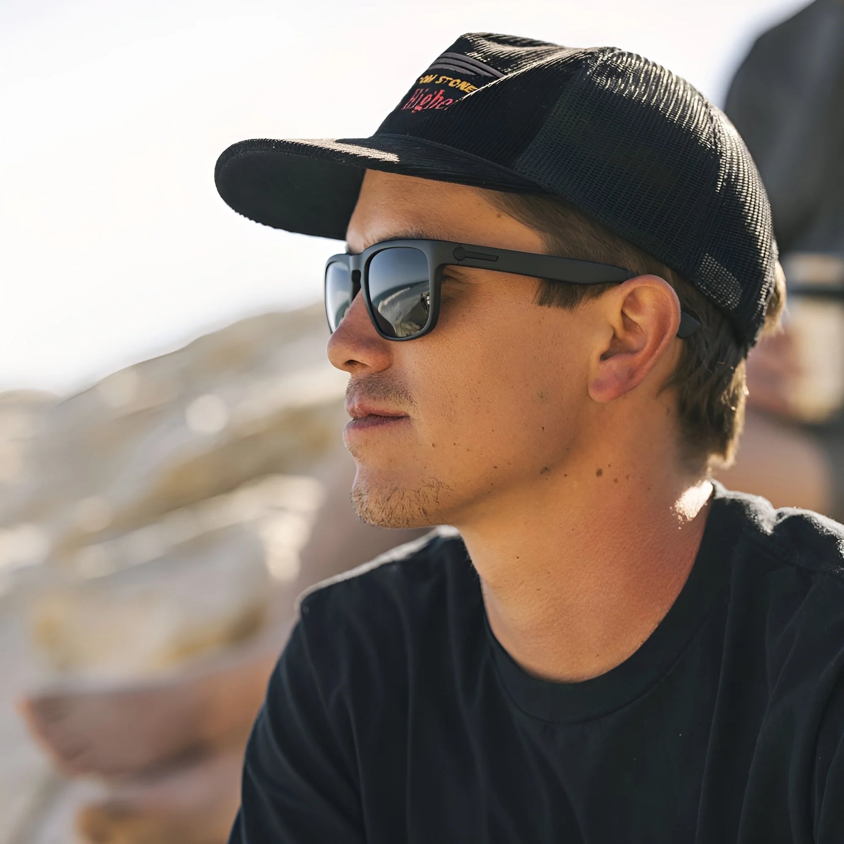 A man wearing Electric Knoxville XL Sunglasses | Size 61 by Electric and a black cap sits outdoors on a sunny day, enjoying superior sun protection and a lightweight fit. A man wearing Electric Knoxville XL Sunglasses | Size 61 by Electric and a black cap sits outdoors on a sunny day, enjoying superior sun protection and a lightweight fit.
