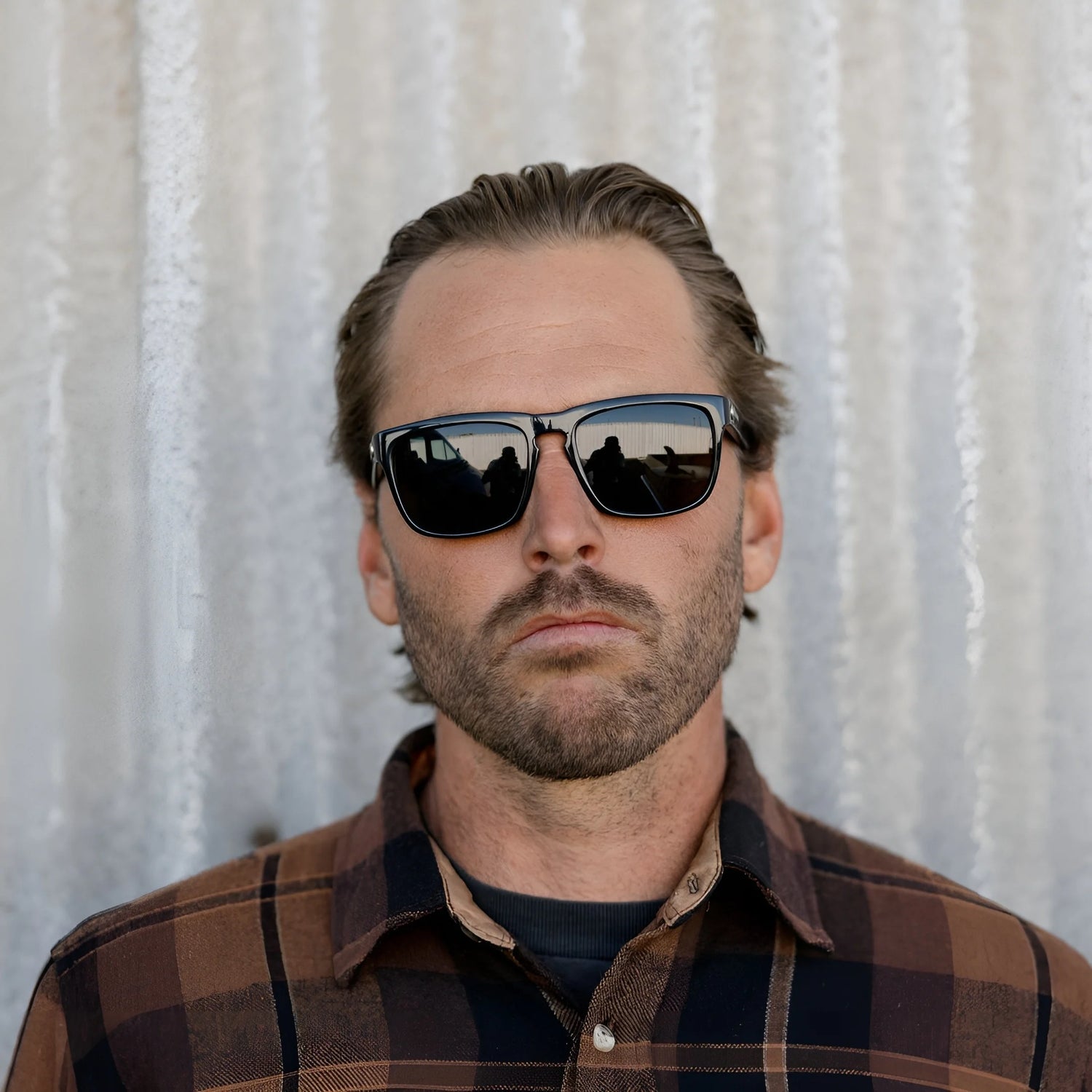 A man in a plaid shirt stands before a corrugated metal wall, sporting Electric Knoxville XL Sunglasses | Size 61 by Electric, highlighting their superior sun protection and lightweight comfort. A man in a plaid shirt stands before a corrugated metal wall, sporting Electric Knoxville XL Sunglasses | Size 61 by Electric, highlighting their superior sun protection and lightweight comfort.