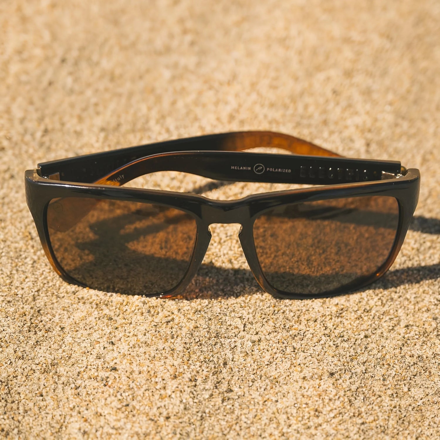 Electric Knoxville XL Sunglasses | Size 61 by Electric feature brown lenses and a lightweight design, resting on sandy ground under bright sunlight while offering superior sun protection. Electric Knoxville XL Sunglasses | Size 61 by Electric feature brown lenses and a lightweight design, resting on sandy ground under bright sunlight while offering superior sun protection.