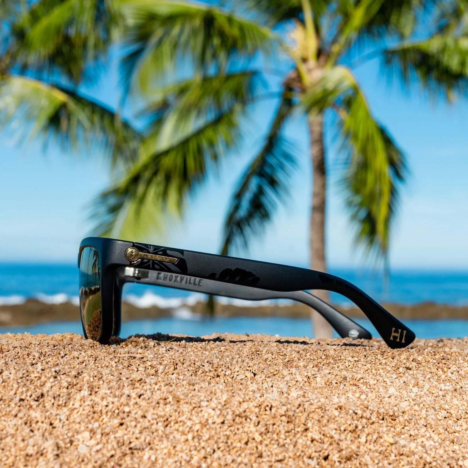 Electric Knoxville XL Sunglasses | Size 61 by Electric rest on sand, providing superior sun protection with a lightweight fit, as palm trees and the ocean form a soft-focus backdrop. Electric Knoxville XL Sunglasses | Size 61 by Electric rest on sand, providing superior sun protection with a lightweight fit, as palm trees and the ocean form a soft-focus backdrop.