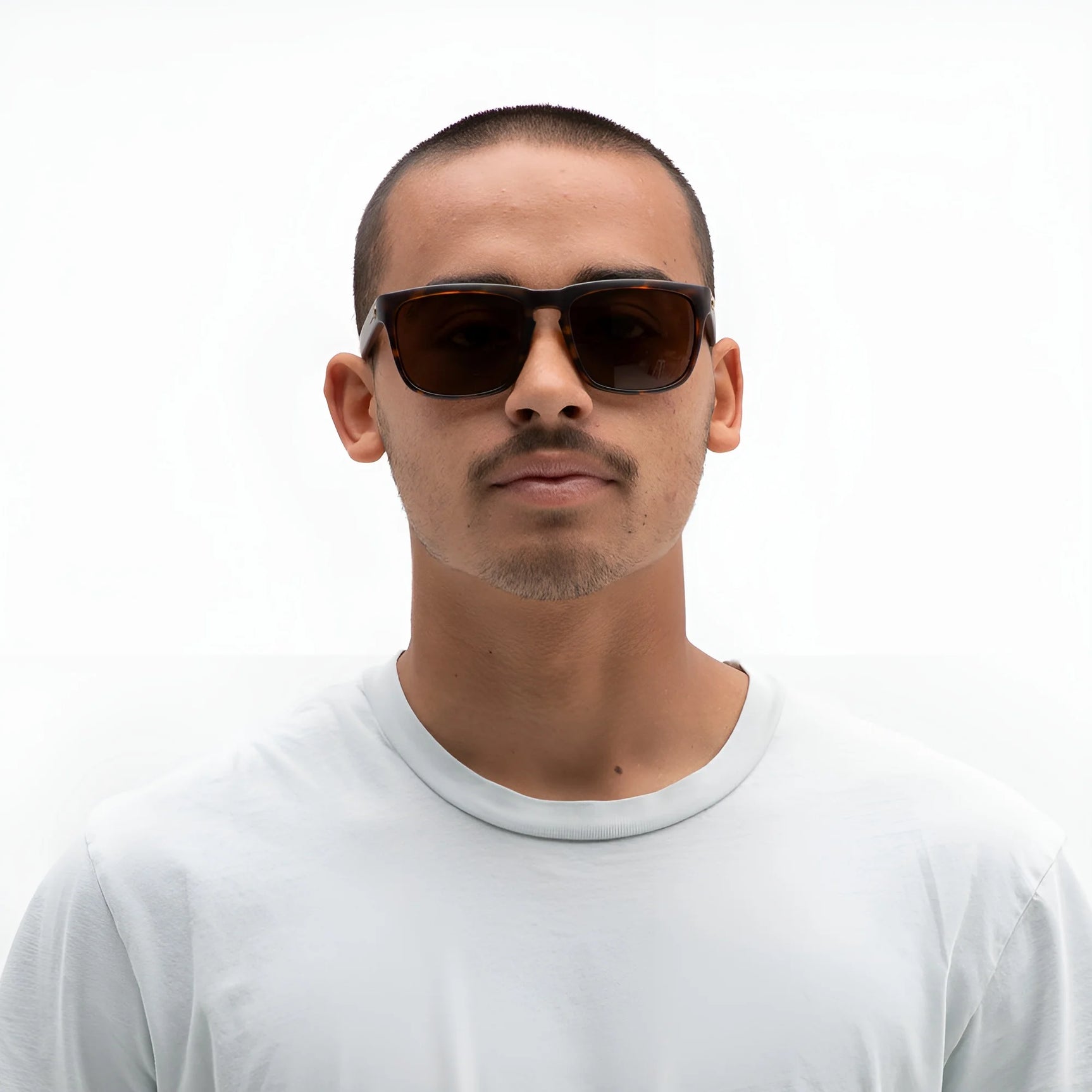A man wearing Electric Knoxville XL Sunglasses (Size 61) by Electric and a white t-shirt stands against a plain white background, showcasing superior sun protection and a lightweight fit. A man wearing Electric Knoxville XL Sunglasses (Size 61) by Electric and a white t-shirt stands against a plain white background, showcasing superior sun protection and a lightweight fit.