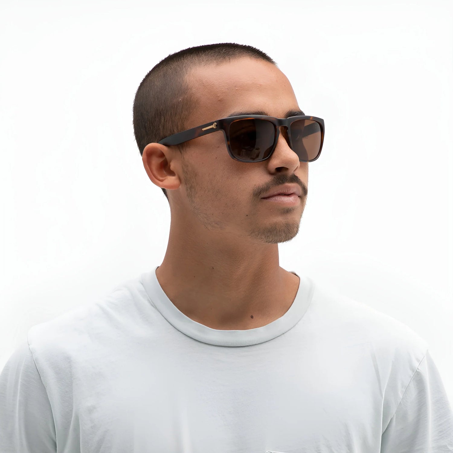 A man with short hair wears Electric Knoxville XL Sunglasses | Size 61 by Electric and a lightweight, light gray t-shirt, standing against a white background to showcase superior sun protection. A man with short hair wears Electric Knoxville XL Sunglasses | Size 61 by Electric and a lightweight, light gray t-shirt, standing against a white background to showcase superior sun protection.