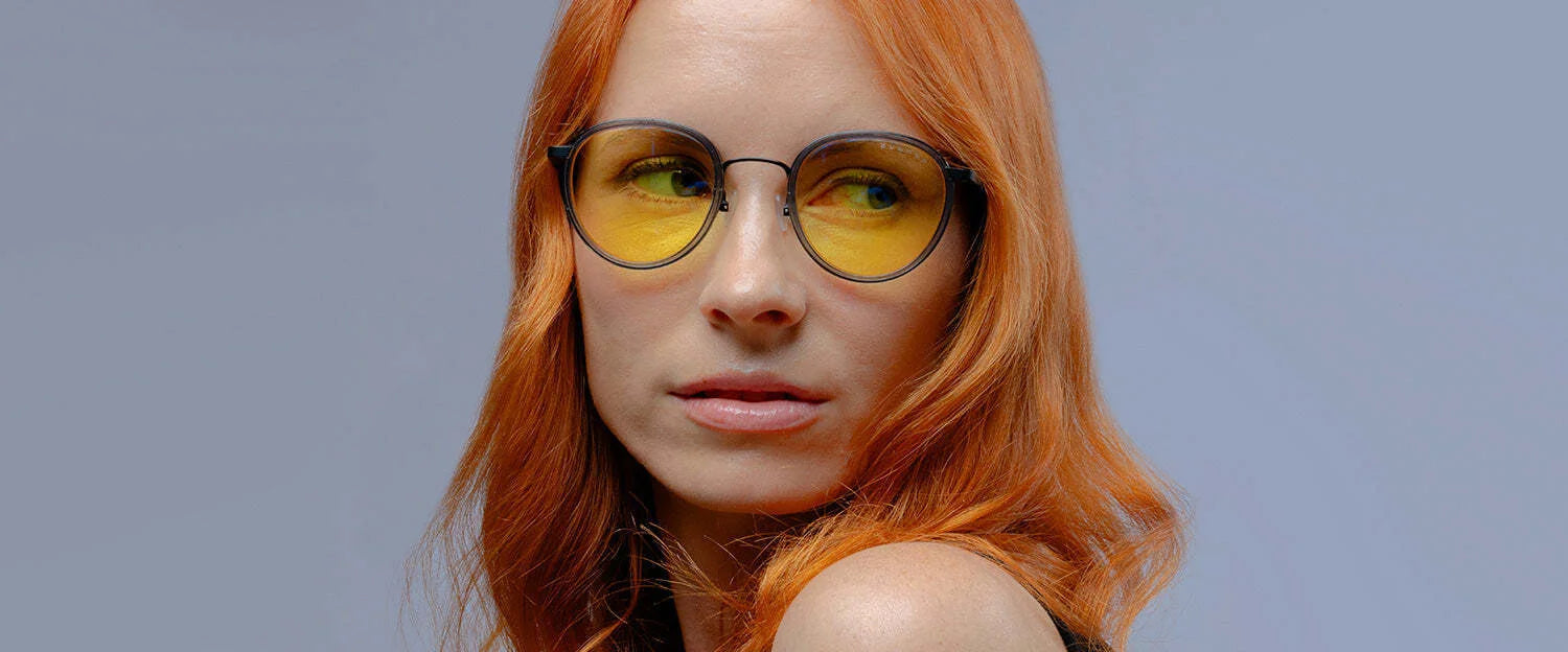 A person with long red hair wears round, yellow-tinted Gunnar Atherton Computer Glasses (Size 48), featuring GUNNAR lens technology, and gazes to the side against a gray background. A person with long red hair wears round, yellow-tinted Gunnar Atherton Computer Glasses (Size 48), featuring GUNNAR lens technology, and gazes to the side against a gray background.