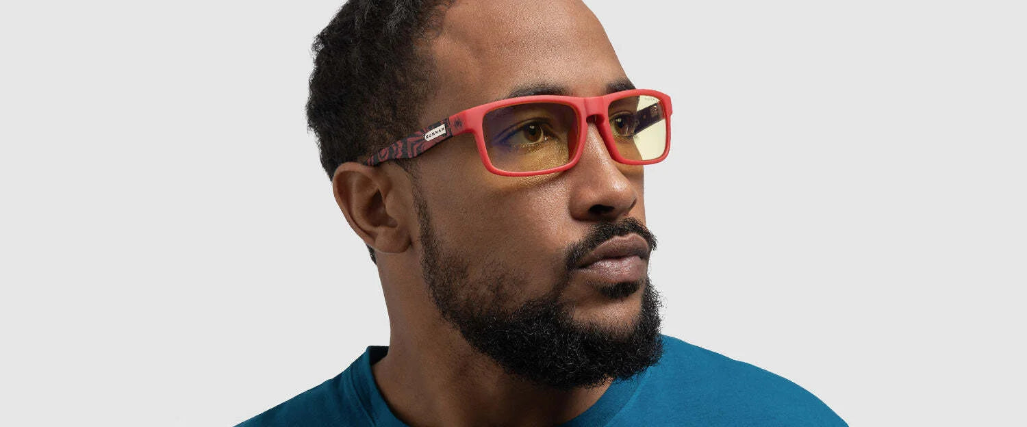 A man in a blue shirt and red-framed Gunnar Enigma Spider-Man Miles Morales Edition Computer Glasses with yellow lenses, known for their durable nylon frame and blue light protection, looks aside against a gray background. A man in a blue shirt and red-framed Gunnar Enigma Spider-Man Miles Morales Edition Computer Glasses with yellow lenses, known for their durable nylon frame and blue light protection, looks aside against a gray background.