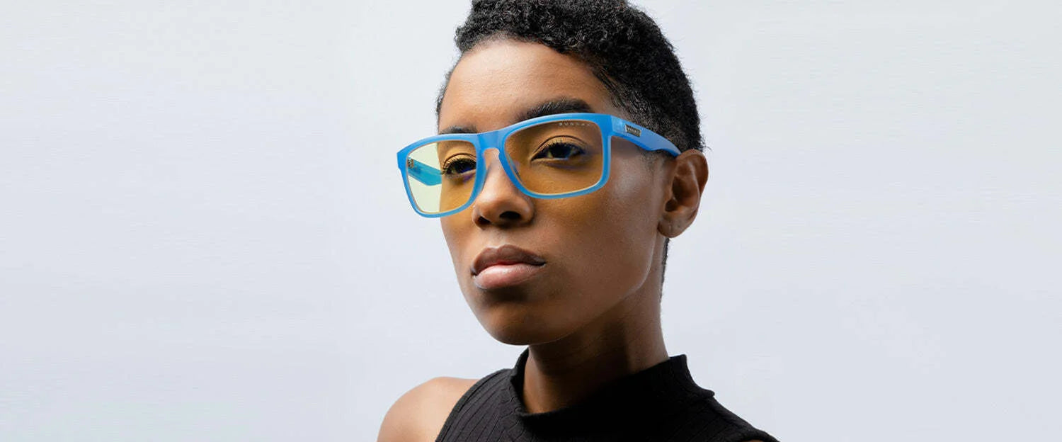 A person wearing Gunnar Intercept Computer Glasses in blue, featuring Blue Light Protection, clad in a black top, gazes thoughtfully to the side against a plain background. A person wearing Gunnar Intercept Computer Glasses in blue, featuring Blue Light Protection, clad in a black top, gazes thoughtfully to the side against a plain background.