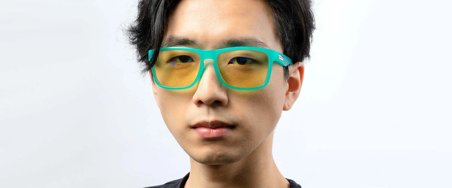 A person with dark hair wears teal Gunnar Intercept Computer Glasses, size 58, featuring yellow lenses for blue light protection, against a plain background. A person with dark hair wears teal Gunnar Intercept Computer Glasses, size 58, featuring yellow lenses for blue light protection, against a plain background.