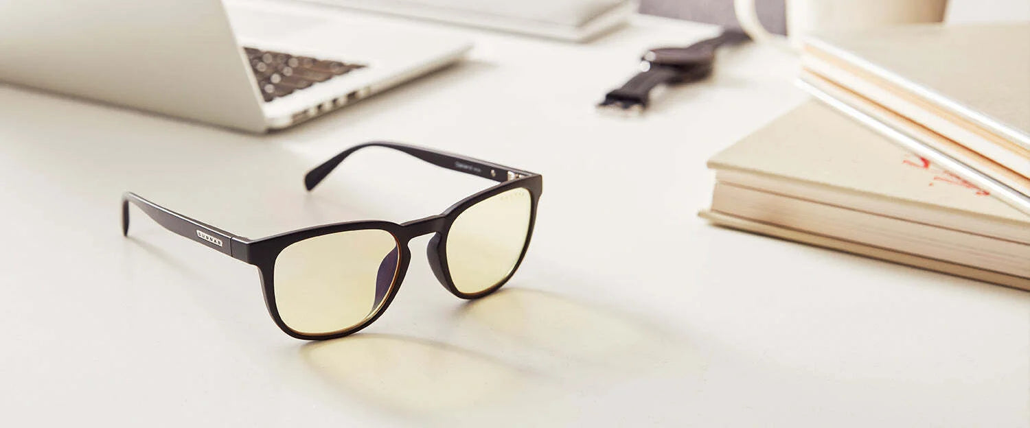 Black-rimmed Gunnar Oakland Computer Glasses (Size 53) with yellow lenses and a durable nylon frame sit stylishly on a white desk near a laptop, books, cup, and watch. These glasses offer excellent blue light protection while keeping you comfortable and stylish. Black-rimmed Gunnar Oakland Computer Glasses (Size 53) with yellow lenses and a durable nylon frame sit stylishly on a white desk near a laptop, books, cup, and watch. These glasses offer excellent blue light protection while keeping you comfortable and stylish.