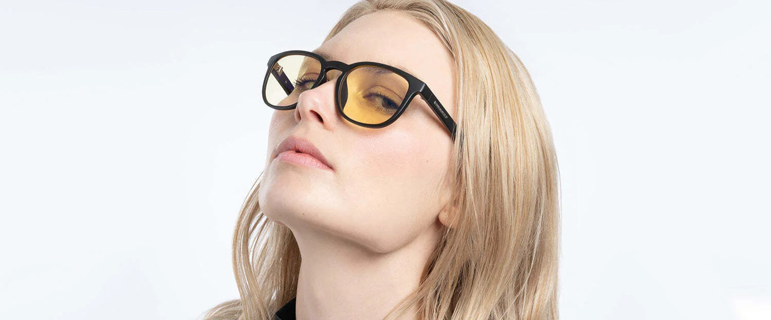 A person with long blond hair wearing GUNNAR's Oakland Computer Glasses, Size 53, looks upward against a plain background. These tinted glasses from Gunnar offer blue light protection. A person with long blond hair wearing GUNNAR's Oakland Computer Glasses, Size 53, looks upward against a plain background. These tinted glasses from Gunnar offer blue light protection.