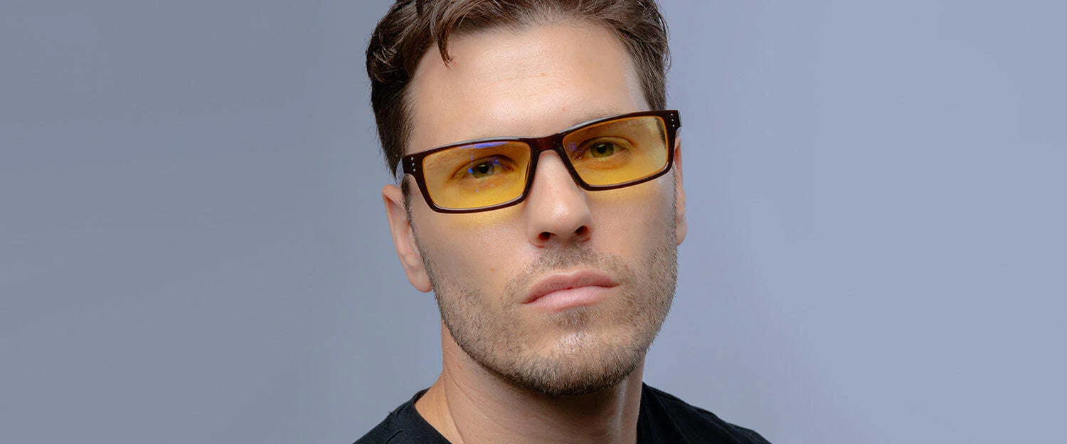 A person wearing Gunnar Riot Computer Glasses with a nylon frame and yellow tint, paired with a black shirt on a neutral background. A person wearing Gunnar Riot Computer Glasses with a nylon frame and yellow tint, paired with a black shirt on a neutral background.