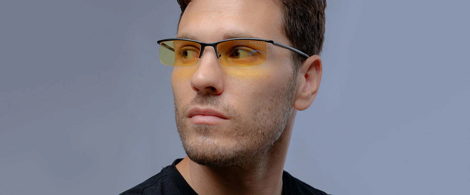 A man in a black shirt gazes sideways while wearing Gunnar Emissary Computer Glasses. These blue light blocking glasses from Gunnar feature yellow-tinted lenses that enhance clarity and provide UV protection. A man in a black shirt gazes sideways while wearing Gunnar Emissary Computer Glasses. These blue light blocking glasses from Gunnar feature yellow-tinted lenses that enhance clarity and provide UV protection.