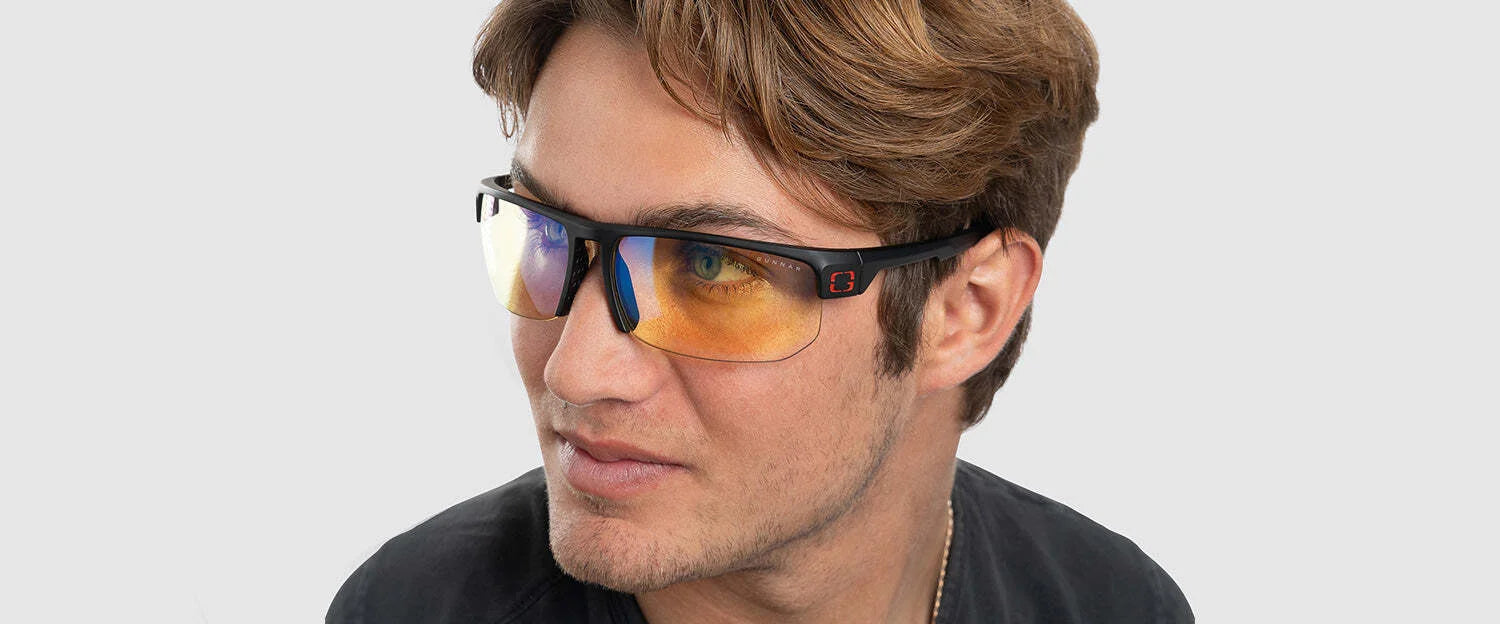 A man wears Gunnar Torpedo 360 Computer Glasses, featuring tinted, interchangeable lenses, and gazes thoughtfully to the side against a plain background. A man wears Gunnar Torpedo 360 Computer Glasses, featuring tinted, interchangeable lenses, and gazes thoughtfully to the side against a plain background.