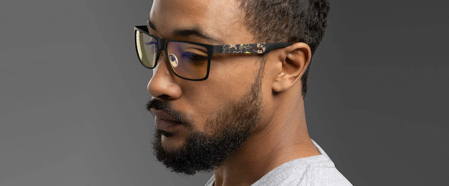 A person with short hair and a beard wearing Gunnar Call of Duty UAV Edition Computer Glasses, featuring an aluminum-magnesium forged frame, looks down against a gray background. A person with short hair and a beard wearing Gunnar Call of Duty UAV Edition Computer Glasses, featuring an aluminum-magnesium forged frame, looks down against a gray background.