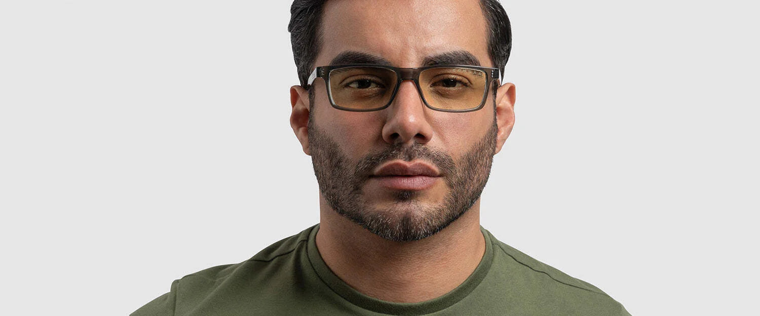 A man in a green shirt wearing Gunnar Vertex Reading Computer Glasses with G-Shield lens coating stares straight ahead against a light gray background, showcasing style and blue light protection. A man in a green shirt wearing Gunnar Vertex Reading Computer Glasses with G-Shield lens coating stares straight ahead against a light gray background, showcasing style and blue light protection.