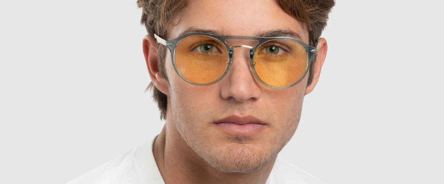 Wearing Gunnar World of Warcraft Alliance Edition Computer Glasses with round yellow-tinted blue light blocking lenses, a person elegantly pairs them with a white shirt against a light gray background. Wearing Gunnar World of Warcraft Alliance Edition Computer Glasses with round yellow-tinted blue light blocking lenses, a person elegantly pairs them with a white shirt against a light gray background.