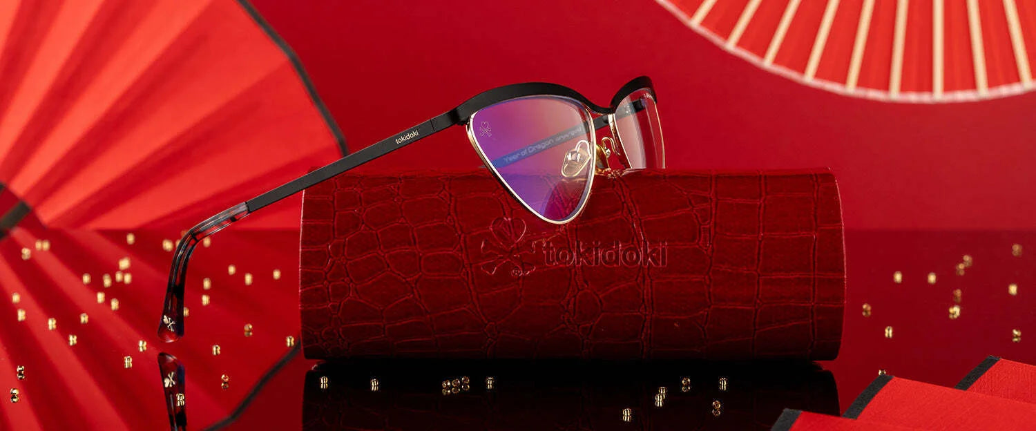 Gunnar Tokidoki Year of the Dragon Computer Glasses, Size 52, elegantly displayed on a red case against a bold red geometric backdrop with scattered gold beads. Gunnar Tokidoki Year of the Dragon Computer Glasses, Size 52, elegantly displayed on a red case against a bold red geometric backdrop with scattered gold beads.