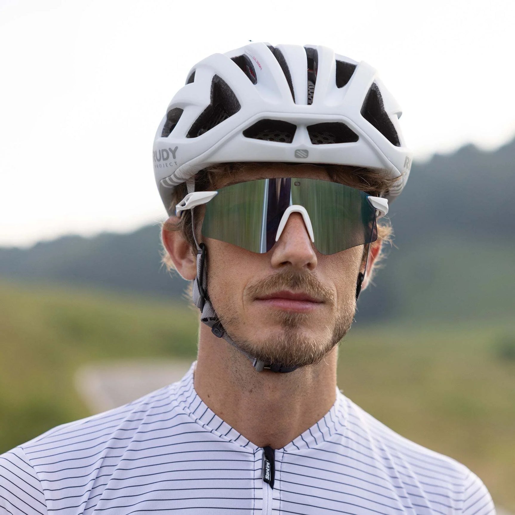 Man outdoors in a striped cycling jersey, wearing a white helmet and Rudy Project Astral Sunglasses (Size 147) with UV protection. Man outdoors in a striped cycling jersey, wearing a white helmet and Rudy Project Astral Sunglasses (Size 147) with UV protection.