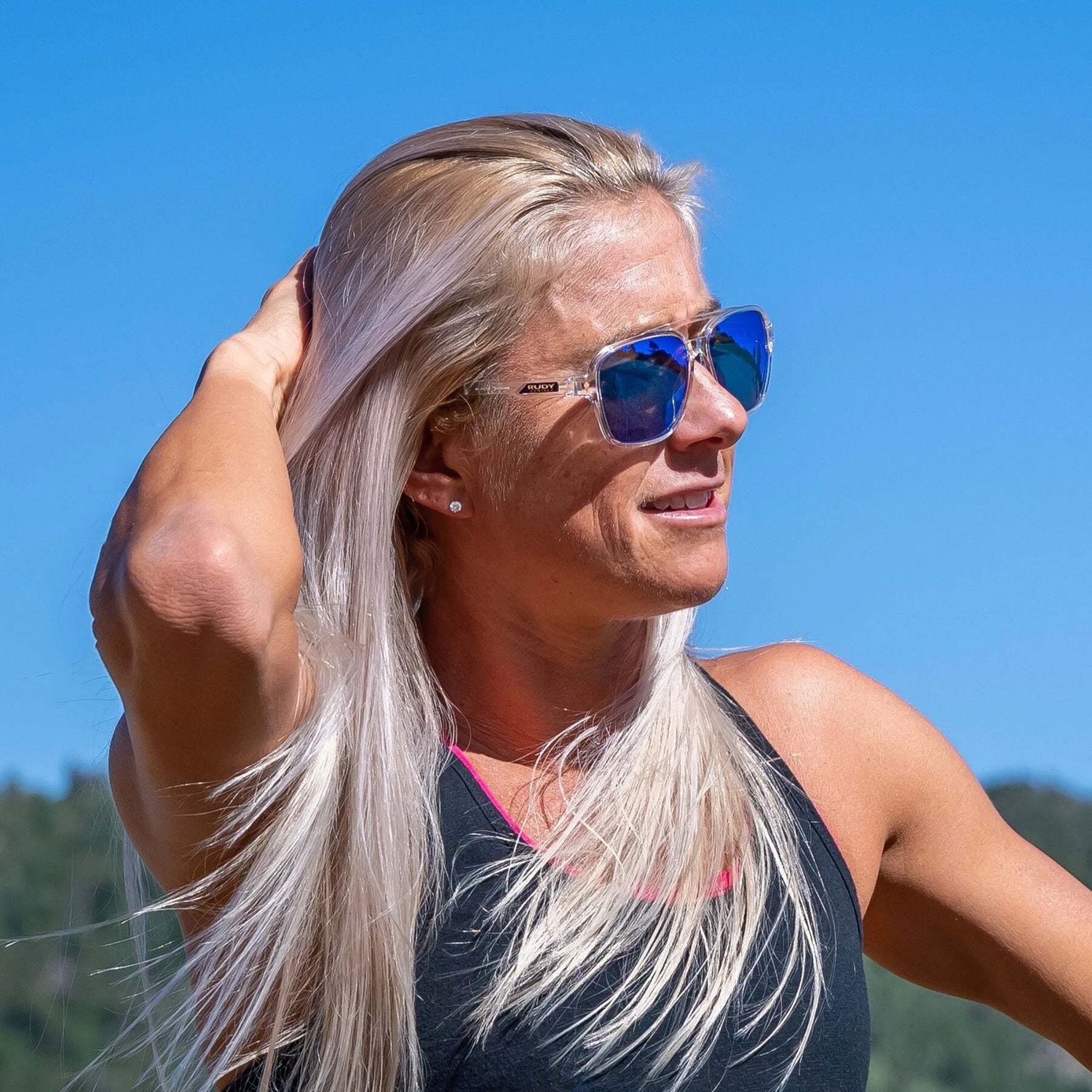 Blonde woman outdoors in Rudy Project Croze Sunglasses | Size 57, touching her hair under a blue sky, enjoys UV protection from Rudy Project. Blonde woman outdoors in Rudy Project Croze Sunglasses | Size 57, touching her hair under a blue sky, enjoys UV protection from Rudy Project.