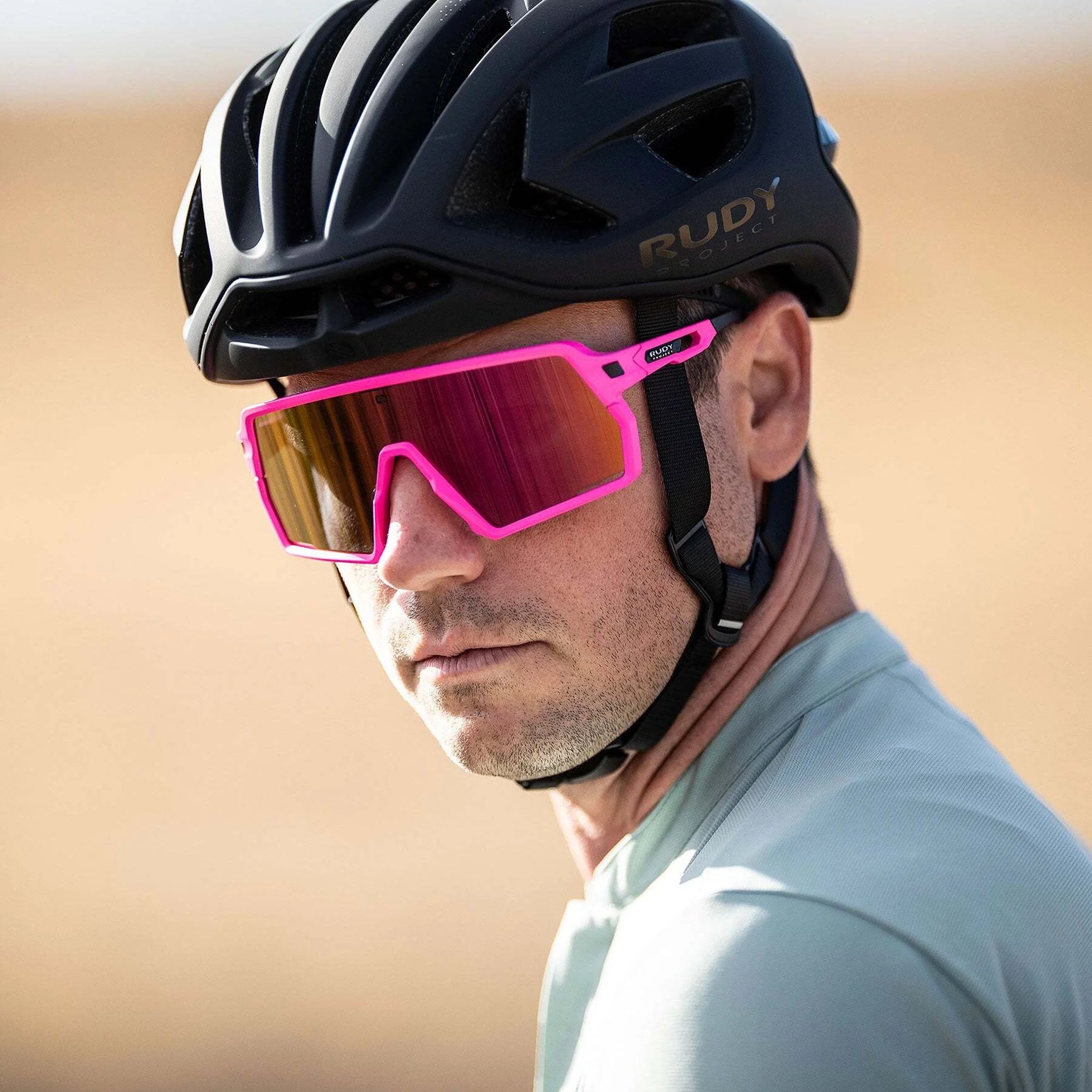 Man wearing Rudy Project Kelion Sunglasses (Size 144) with UV protection and a black bike helmet, looking sideways outdoors. Man wearing Rudy Project Kelion Sunglasses (Size 144) with UV protection and a black bike helmet, looking sideways outdoors.