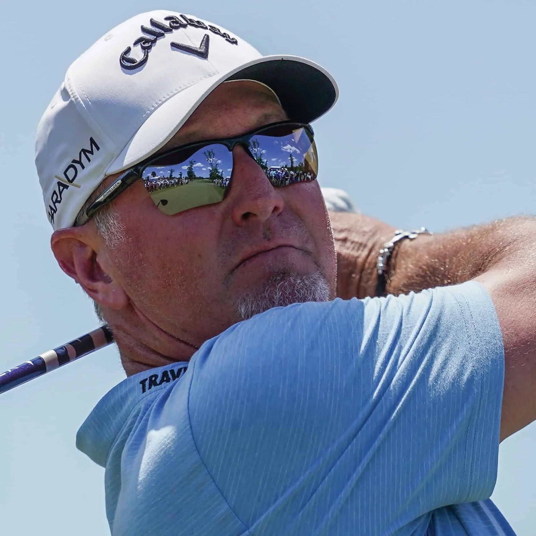 A person in Scheyden CIA GRABBER sunglasses with TR90 composite frames and a cap, holding a golf club mid-swing under the clear blue sky. A person in Scheyden CIA GRABBER sunglasses with TR90 composite frames and a cap, holding a golf club mid-swing under the clear blue sky.