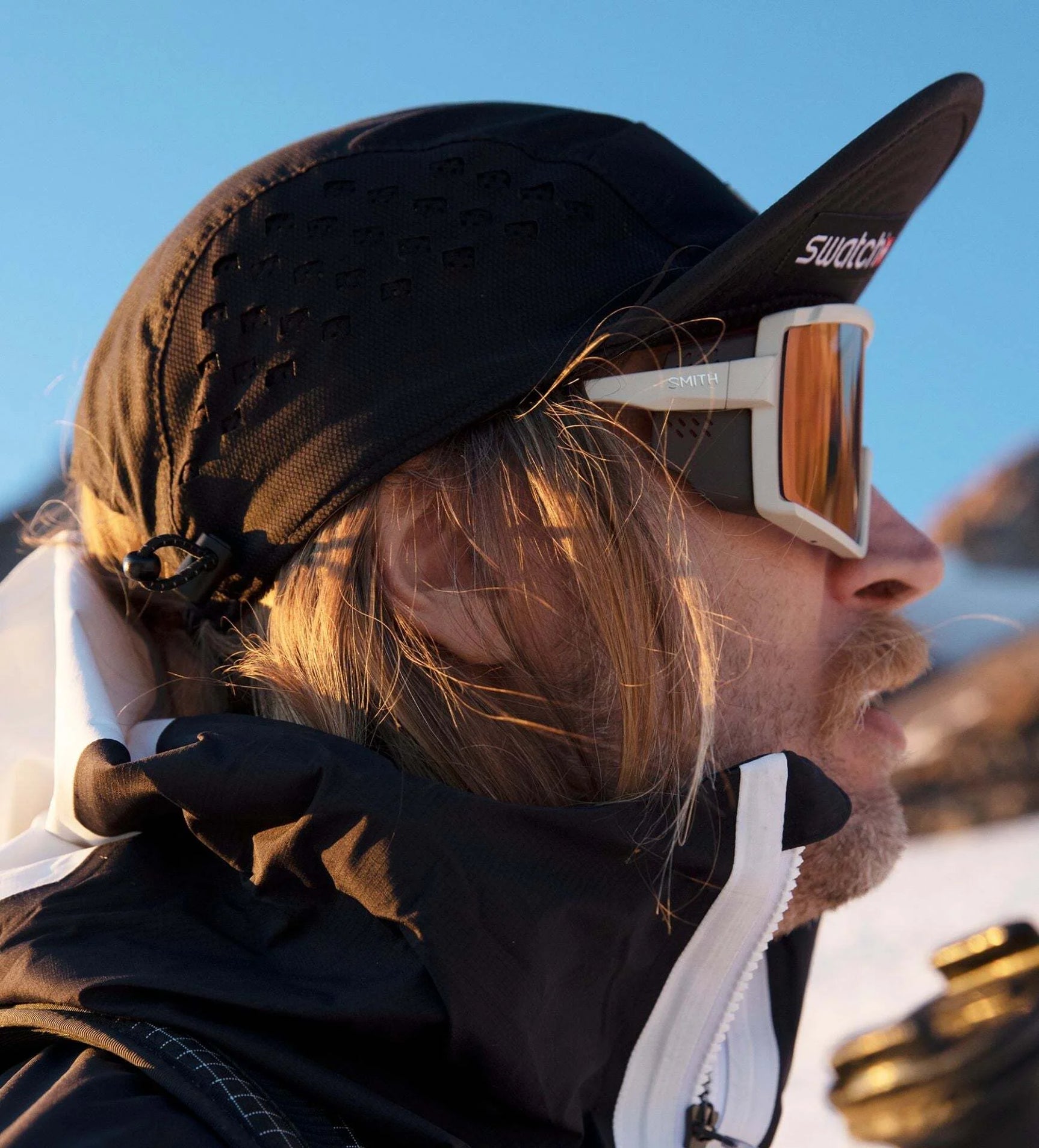 A person wearing Smith Optics Pursuit Sunglasses with ChromaPop™ lenses, dressed in a black jacket, stands against a snowy mountain backdrop. A person wearing Smith Optics Pursuit Sunglasses with ChromaPop™ lenses, dressed in a black jacket, stands against a snowy mountain backdrop.