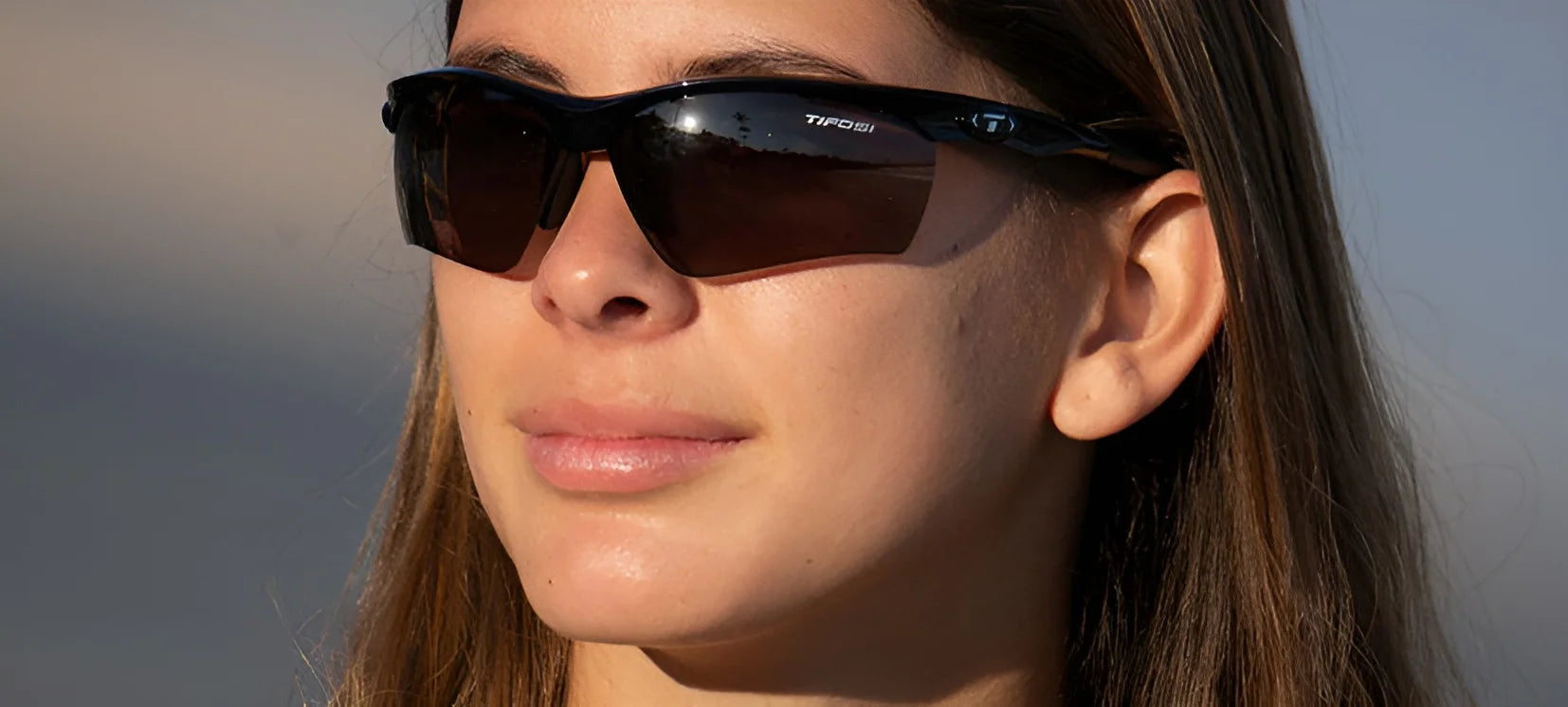 A person wearing Tifosi Optics VERO Sunglasses, designed for smaller faces, gazes into the distance on a sunny day. A person wearing Tifosi Optics VERO Sunglasses, designed for smaller faces, gazes into the distance on a sunny day.