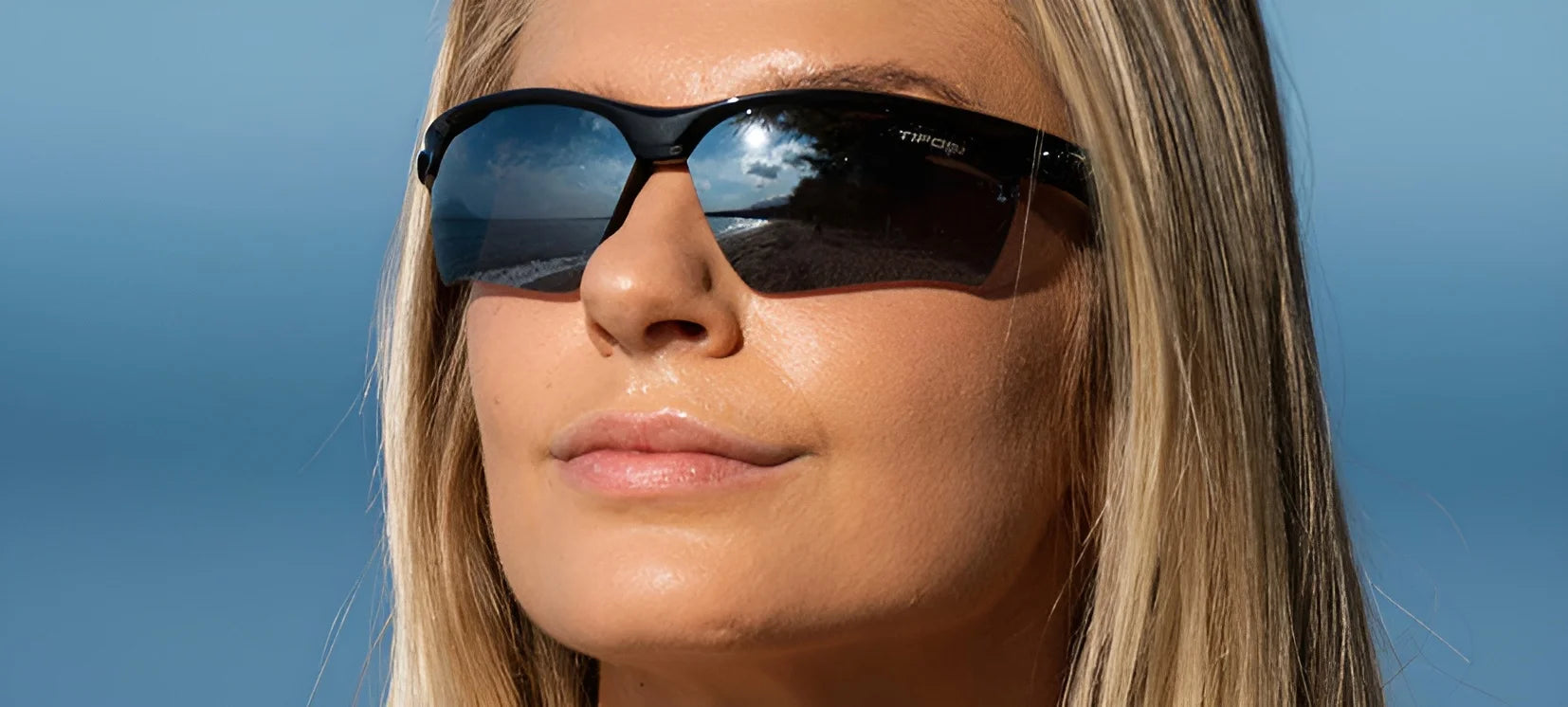 A person wearing Tifosi Optics VERO Sunglasses | Size 64 stands before a blue sky, the lenses reflecting a stunning landscape backdrop, ideal for multi-sport enthusiasts. A person wearing Tifosi Optics VERO Sunglasses | Size 64 stands before a blue sky, the lenses reflecting a stunning landscape backdrop, ideal for multi-sport enthusiasts.