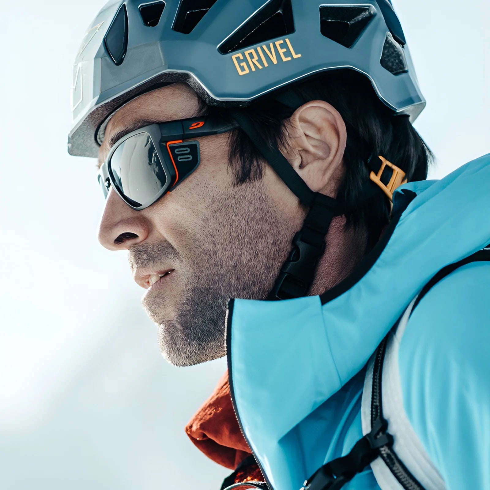 A person in a blue jacket and helmet, wearing Julbo Shield Sunglasses featuring Grip Nose technology, looks ahead outdoors. A person in a blue jacket and helmet, wearing Julbo Shield Sunglasses featuring Grip Nose technology, looks ahead outdoors.