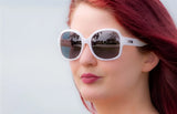 A person with red hair and white DEA Eyewear DESIRE Sunglasses (Size 58) gazes into the distance against a soft background.