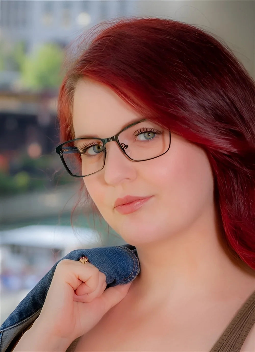 A woman with red hair and DEA Eyewear EYE LOVE eyeglasses in size 58 holds a denim jacket over her shoulder, standing outdoors.