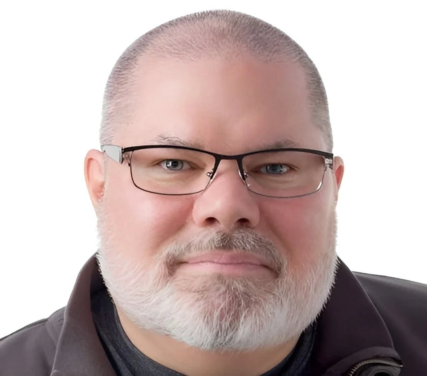 A man with a white beard and a neutral expression, wearing Fatheadz JULIO Eyeglasses in Size 60, which feature a sleek and stylish design, is set against a plain background. His dark jacket complements the look, adding an understated sophistication.