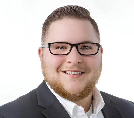 A smiling man with a beard in a suit wears stylish Fatheadz WALLSTREET Eyeglasses, designed for larger head sizes, set against a white background.