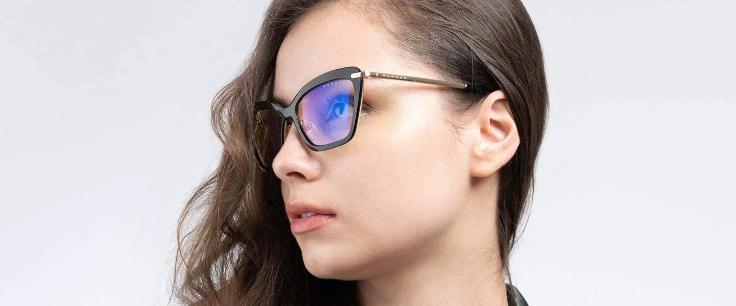 A person with long hair wears Gunnar Anna Computer Glasses (Size 54), featuring stylish, reflective cat-eye frames and GUNNAR lens technology for optimal blue light blocking, against a neutral background.