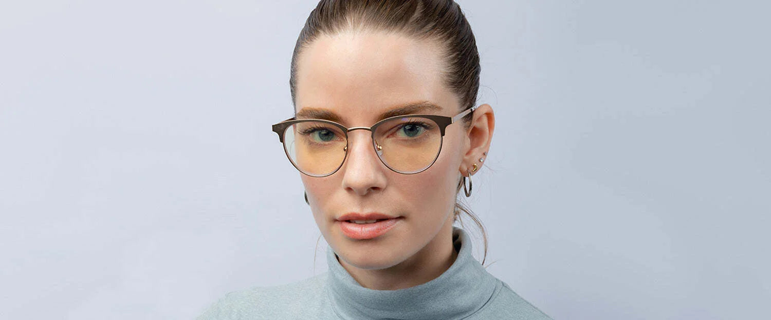 A woman wearing Gunnar Apex Computer Glasses and a light blue turtleneck stands against a pale background, ready to combat digital eye strain.