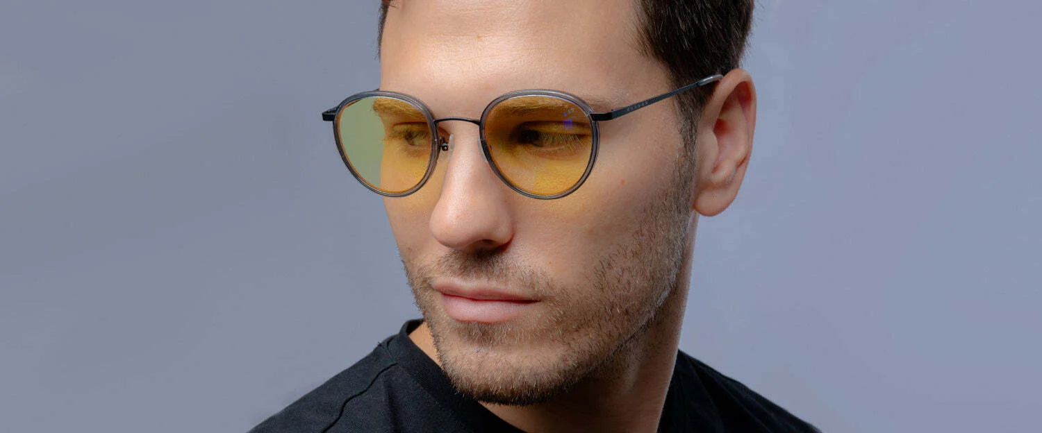 A bearded man wearing Gunnar Atherton Computer Glasses in size 48 with yellow tints and blue light protection gazes to the side against a gray backdrop.