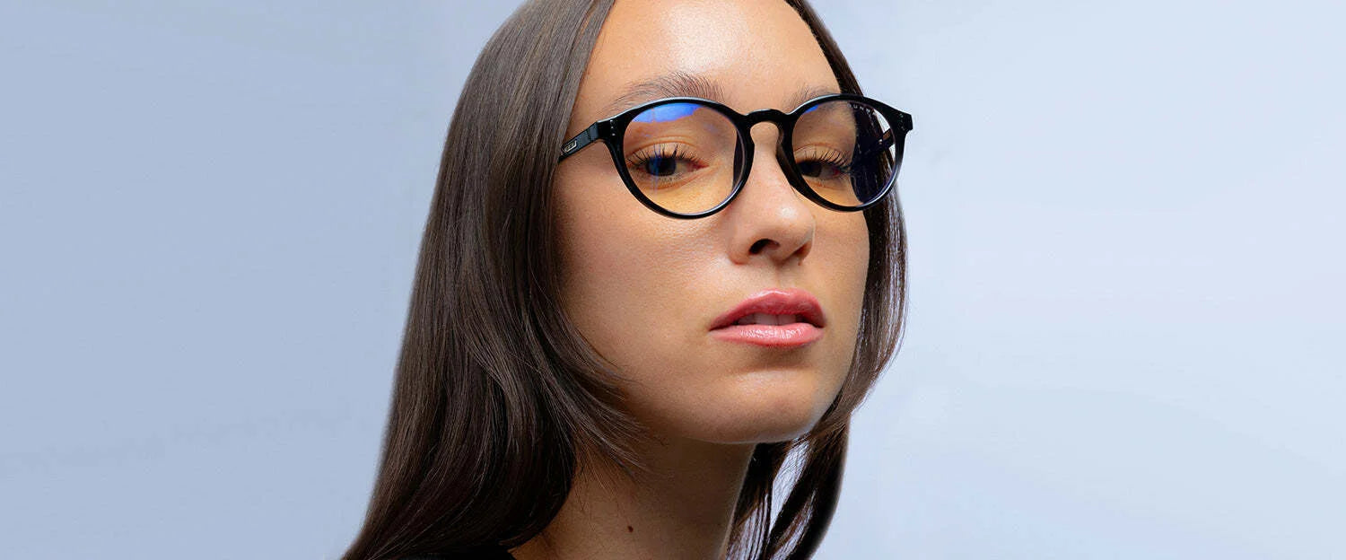A person with long brown hair and a neutral expression against a light blue background, wearing Gunnar Attache Reading Computer Glasses | Size 50, possibly benefiting from their blue light protection.