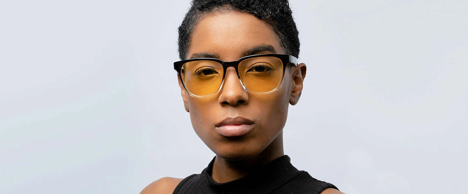 A person wearing Gunnar Berkeley Computer Glasses with yellow-tinted, anti-reflective lenses and a black sleeveless top stands against a light gray background.