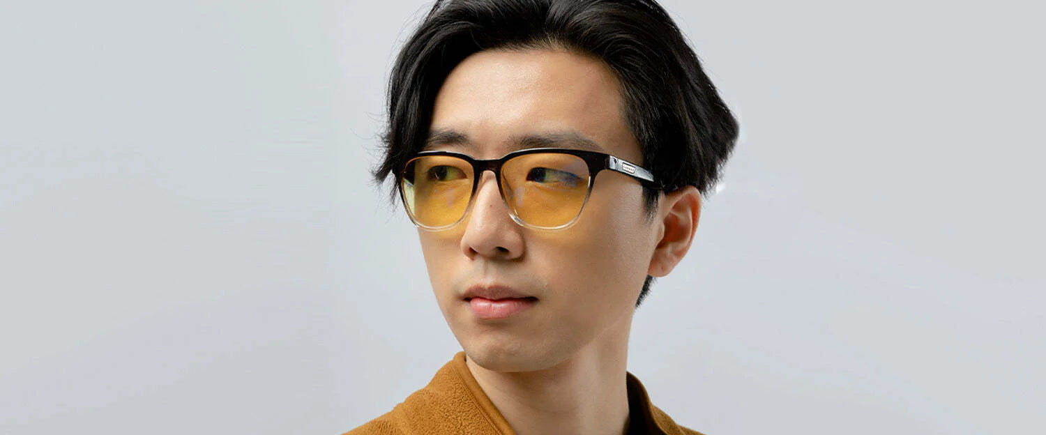 A person wearing Gunnar's Berkeley Computer Glasses in size 54, featuring yellow-tinted lenses for blue light protection, and a brown top, looking to the side against a plain background.