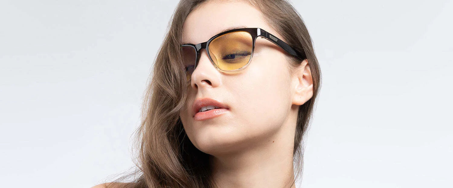 A woman with long brown hair wears Gunnar Berkeley Computer Glasses, size 54, featuring anti-reflective lenses, as she looks down against a light gray background.