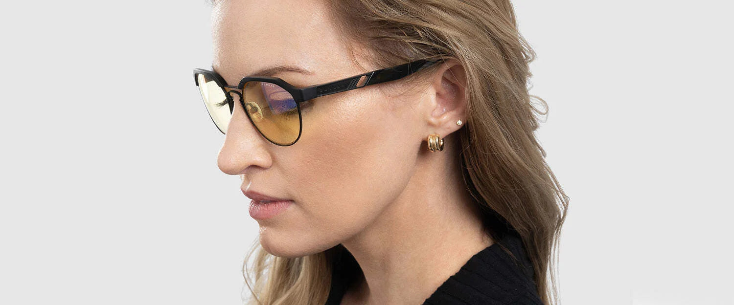 Wearing Gunnar Campbell Computer Glasses (Size 52) with yellow-tinted lenses and gold hoop earrings, a person stands against a plain background, effortlessly combining fashion with function featuring blue light blocking technology.
