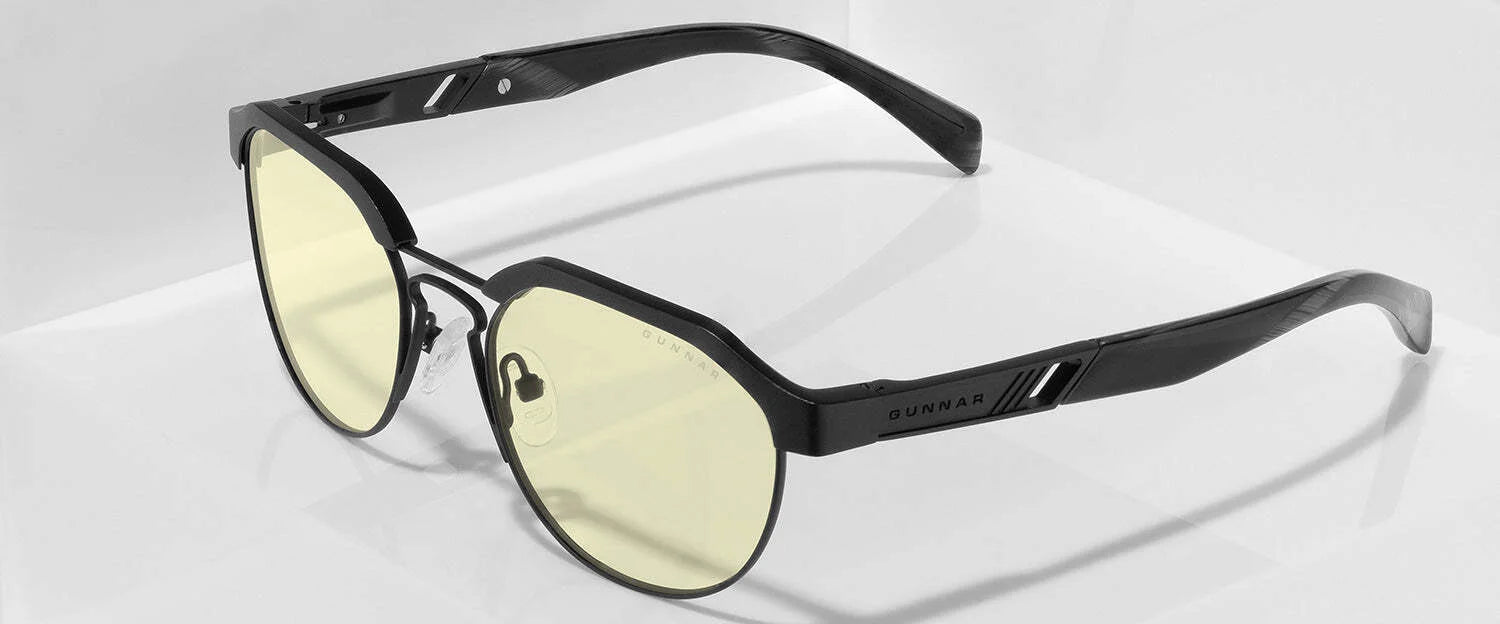 The Gunnar Campbell Computer Glasses (Size 52) feature a sleek black frame with yellow-tinted lenses, offering stylish protection on a reflective white surface thanks to their blue light-blocking technology.