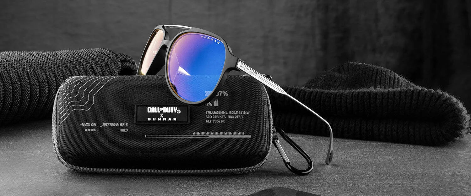 Gunnar Call of Duty Ghost Edition Computer Glasses with blue lenses rest on a black case, accompanied by a black knit hat and sweater.