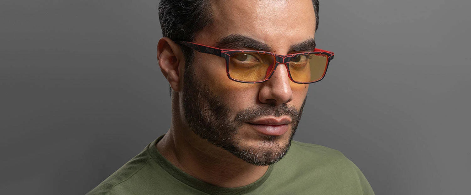 A man with a trimmed beard wears Gunnar Cruz Spider-Man Miles Morales Edition Computer Glasses, sporting orange-tinted blue light protection lenses. He's in a green shirt against a gray background.