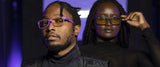 Under purple lighting, two people sport Gunnar's Cruz Black Panther Edition Computer Glasses with durable nylon frames. Their sleek eyewear features Blue Light Protection, perfect for those donning dark attire. One stands in the foreground and one in the background.